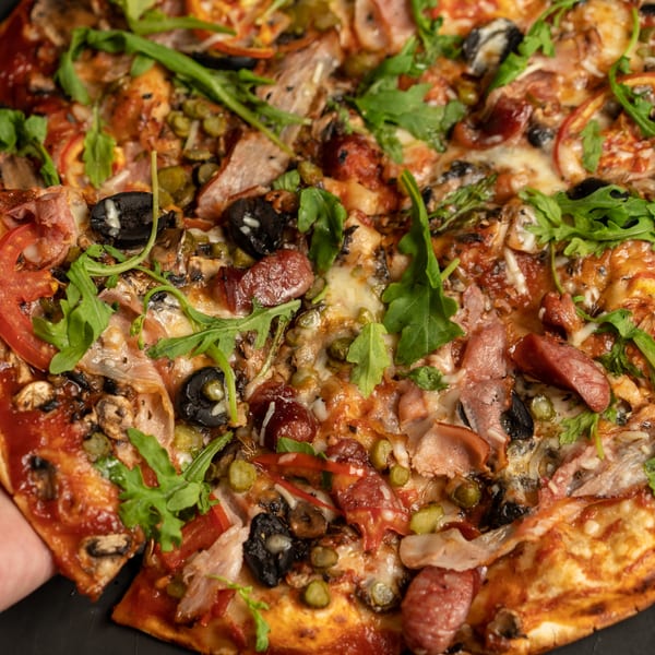 Close-up of a freshly baked Auburn House of Pizza pizza with various toppings and a slice being removed.